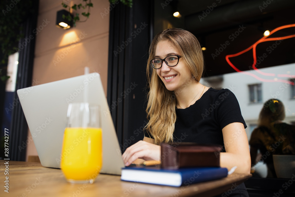 Happy smiling hipster girl in fashionable glasses skilled social media content writer having online video call on laptop computer, sitting in restaurant during recreation time in weekend. Happy smiling hipster girl in fashionable glasses skilled social media content writer having online video call on laptop computer, sitting in restaurant during recreation time in weekend.