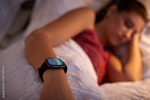 Fotografie Woman Sleeping In Bed With Focus On Smart Watch She Is Wearing