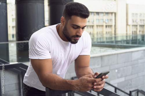 Attractive young man typing on the phone. Front view. 
