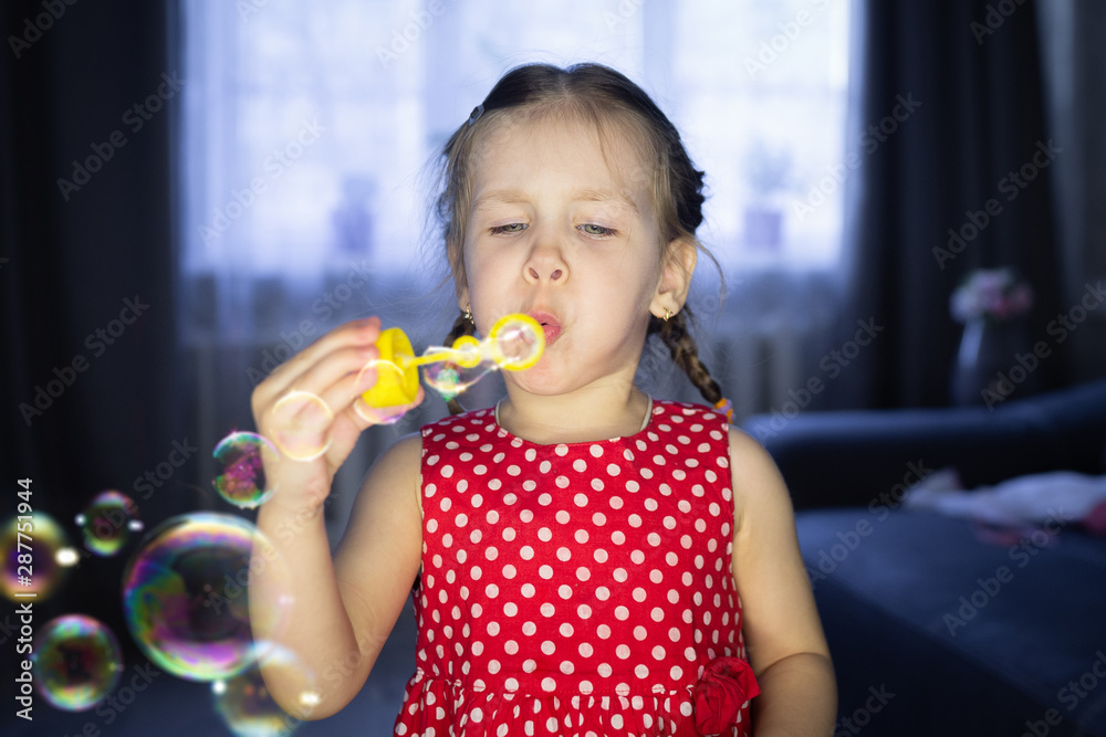 A little girl blowing soap bubbles at home. Children's fun and games A little girl blowing soap bubbles at home. Children's fun and games