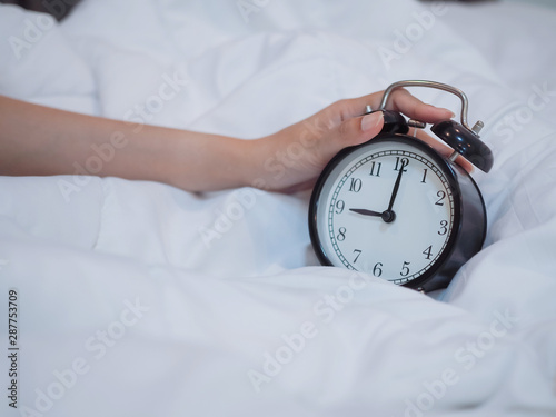 hand holding alarm clock on the bed