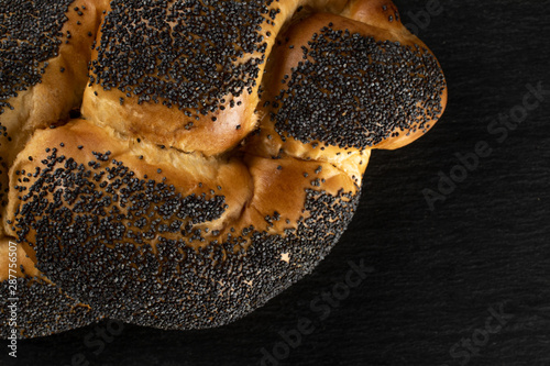 Closeup of one whole twisted poppy seed bun flatlay on grey stone photo