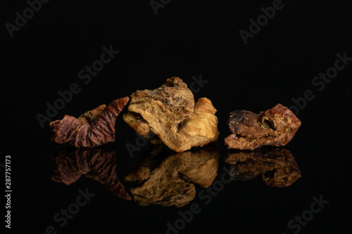 Group of three pieces of roseship with orange rind of lingonberry strawberry fruit tea macro isolated on black glass