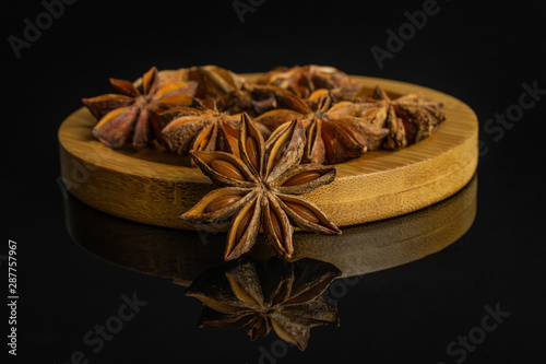 Lot of whole dry brown star anise illicium verum on round bamboo coaster isolated on black glass