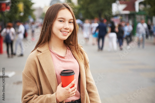 young woman with drink in a paper cup in a city street. Girl with coffee to go.