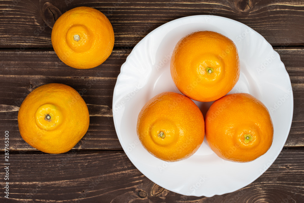 Group of five whole fresh orange tangelo minneola on white ceramic plate flatlay on brown wood Group of five whole fresh orange tangelo minneola on white ceramic plate flatlay on brown wood