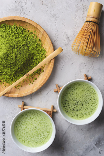 Matcha green tea ,powder matcha on a wooden round plate,welded powder in white Tawan,tasaku and a bamboo whisk on white concrete background