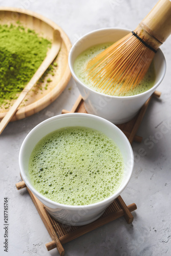 Matcha green tea in two white Tawan, tasaku and a bamboo whisk on white concrete background