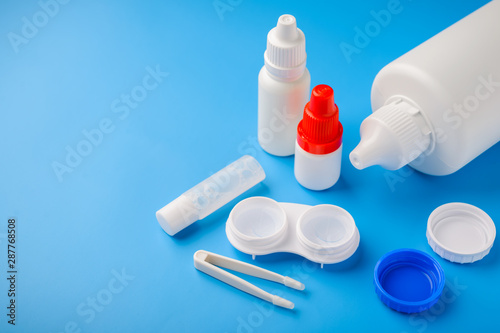 Optical corrective medical soft contact lenses for eyes in white plastic case with storage solution, accessories and care products in plastic bottles on blue background, Cleaning