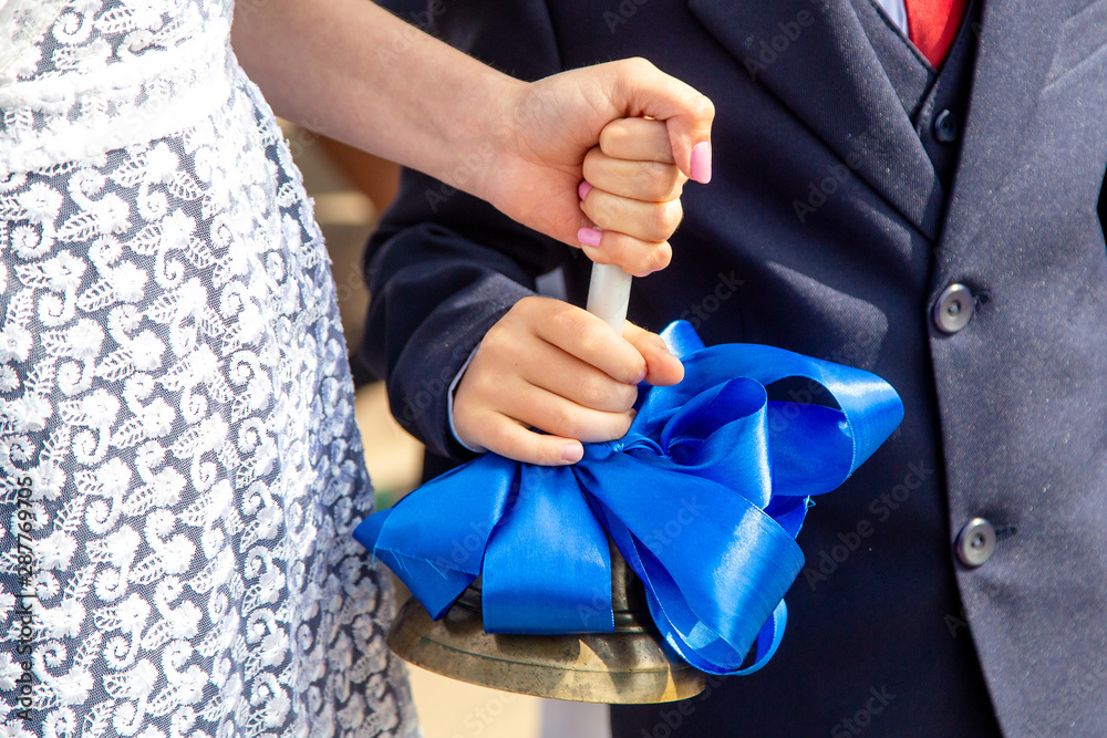 hands of a schoolgirl girl and a first grader boy hold a bell