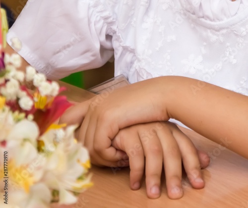 Children's hands folded one on top of another at school desk