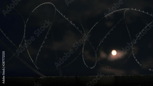 The moon shines through the barbed wire. Timelapce. photo