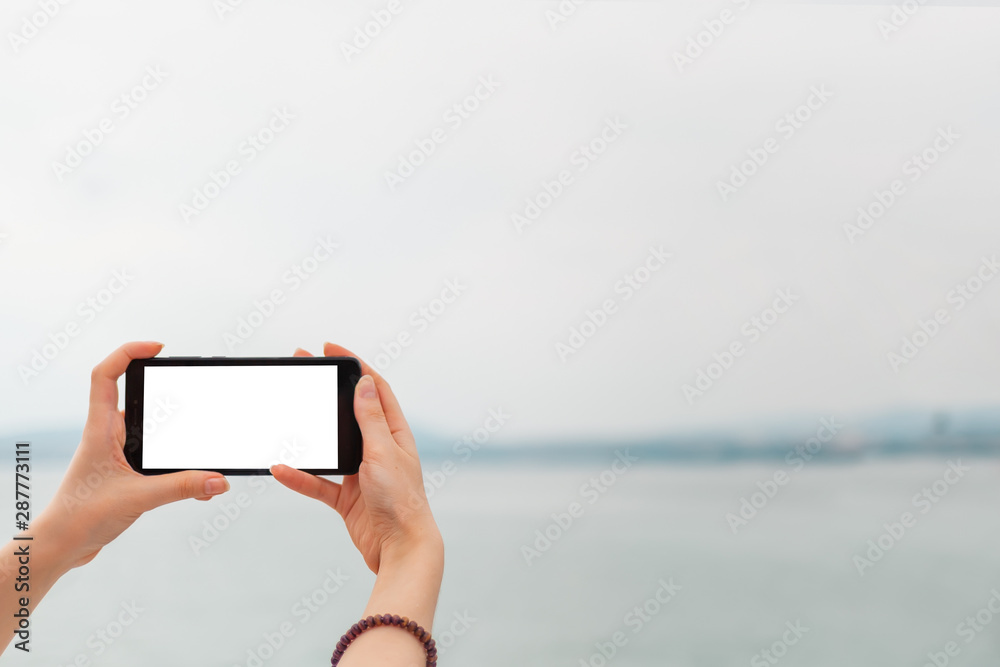 Mock up. Women's hands holding the phone horizontally. In the background sea and sky. Copy space. Isolate
