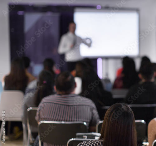 Seminar with expert speaker presenting to audience in hall. Blank business presentation screen for copy space. Executive presenter giving a speech. Leadership training coach in workshop lecture.