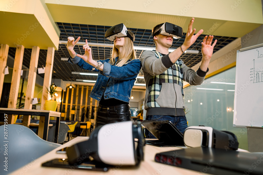 amazed young beautiful couple testing virtual reality 3D video glasses VR headset dressed in casual outfit curious by augmented reality in modern office