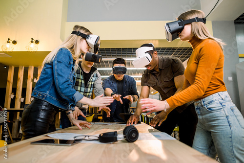 Business people using virtual reality goggles during meeting. Team of multiethnical developers testing virtual reality headset and discussing new ideas to improve the visual experience. photo