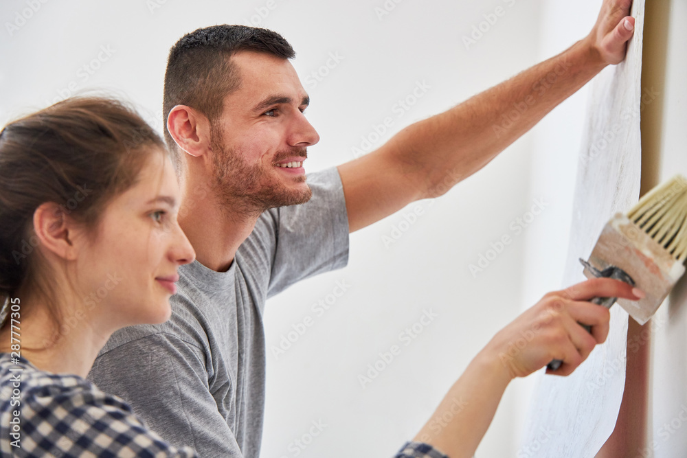 Fototapeta premium Junges Paar beim Tapezieren mit Tapete an Wand