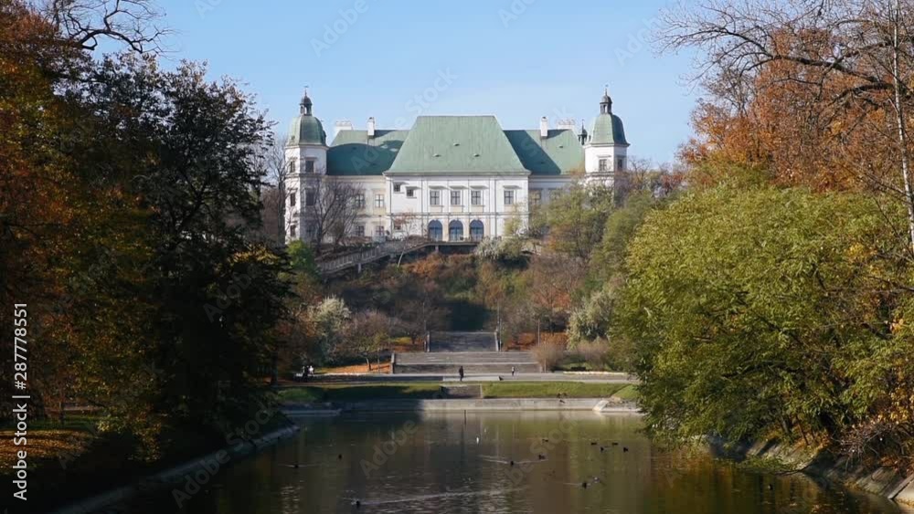 City park Royal Lazienki with pond or lake and Ujazdowski Castle on background with blue sky, trees and fallen leaves at autumn. Warsaw, Poland, Europe. Close-up view City park Royal Lazienki with pond or lake and Ujazdowski Castle on background with blue sky, trees and fallen leaves at autumn. Warsaw, Poland, Europe. Close-up view
