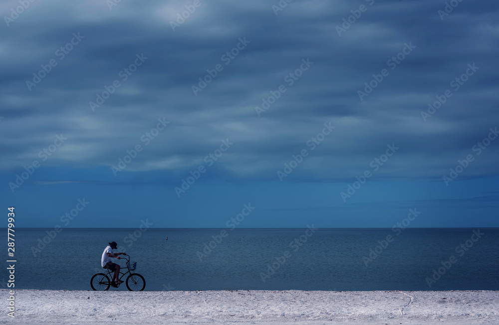 Naklejka premium A cyclist rides on the surf line along the beach. The coast of the ocean, the minimalism of the lines. Florida. USA.
