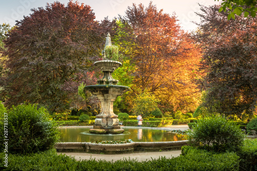 Central fountain of the Botanical Garden of Coimbra, Portugal, on a late spring afternoon, with colorful trees and lit by the sunset.