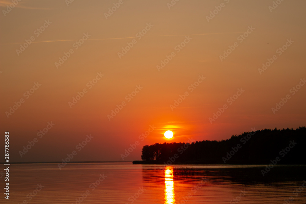 The  horizontal photo of golden sunset above the river or sea. Reflection in the water like fire. Seacoast.