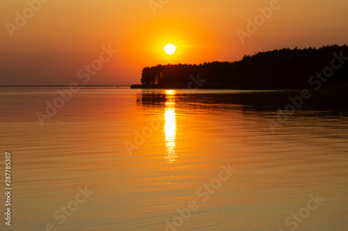 The horizontal photo of golden sunset above the river or sea. Reflection in the water like fire. Seacoast.