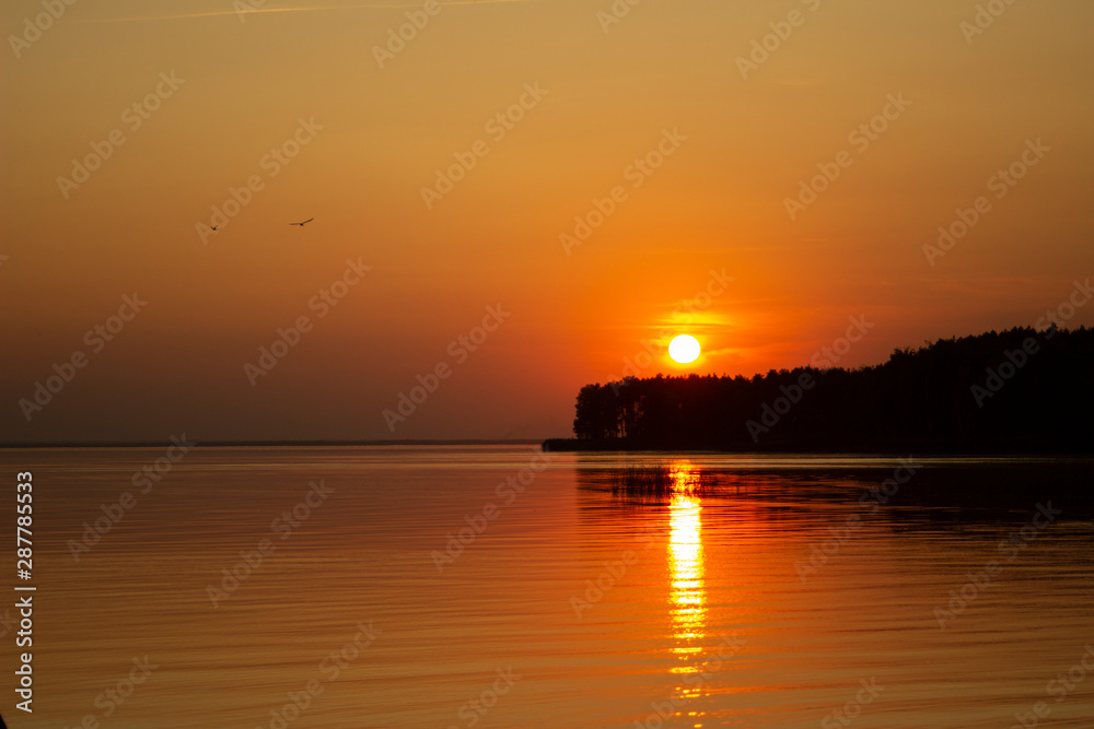 Naklejka premium The horizontal photo of golden sunset above the river or sea. Reflection in the water like fire. Seacoast.