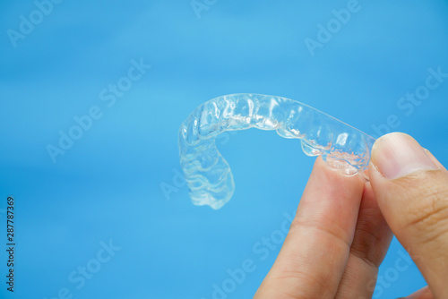 hand holding clear plastic retainer teeth that isolated on blue sky background. it's an equipment for orthodontist give the patient to orthodontic surgery in dental clinic or hospital