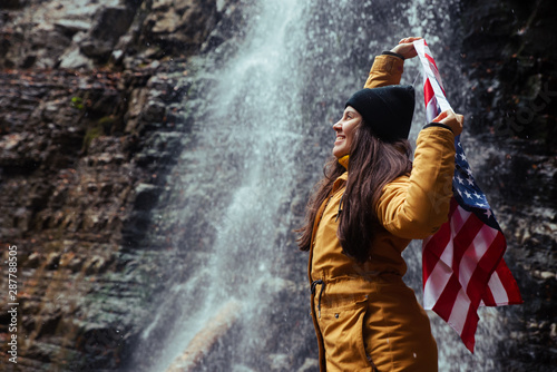 Fototapeta Naklejka Na Ścianę i Meble -  young caucasian adult female with usa flag in front of waterfall