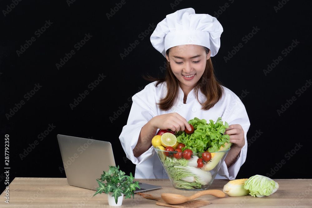 Portrait of a young beautiful Asian woman chef smiling and preparing ingredients for meal or salad by using internet. She was happy and confident .Isolated and studio lighting on black background. Portrait of a young beautiful Asian woman chef smiling and preparing ingredients for meal or salad by using internet. She was happy and confident .Isolated and studio lighting on black background.