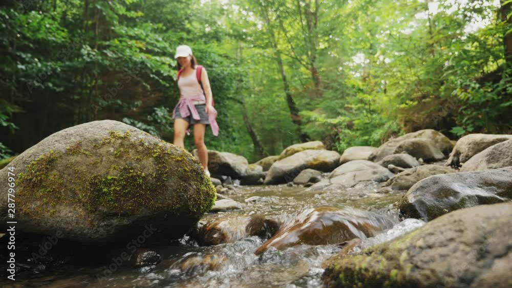 A girl walks on stones along a mountain river in a forest. Legs of young woman stepping over rocks on nature during travel. Low angle of view. Slow-motion 4k video A girl walks on stones along a mountain river in a forest. Legs of young woman stepping over rocks on nature during travel. Low angle of view. Slow-motion 4k video