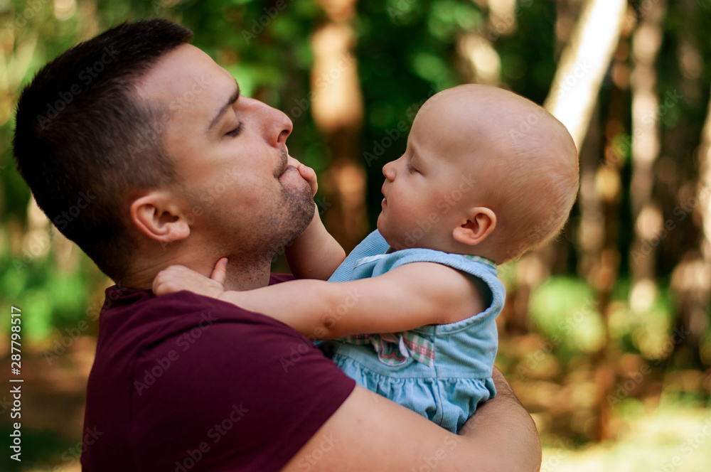 Beautiful young father holds one year old daughter in his arms in the park. Playing with children, learning, happy moment of fatherhood. Beautiful young father holds one year old daughter in his arms in the park. Playing with children, learning, happy moment of fatherhood.