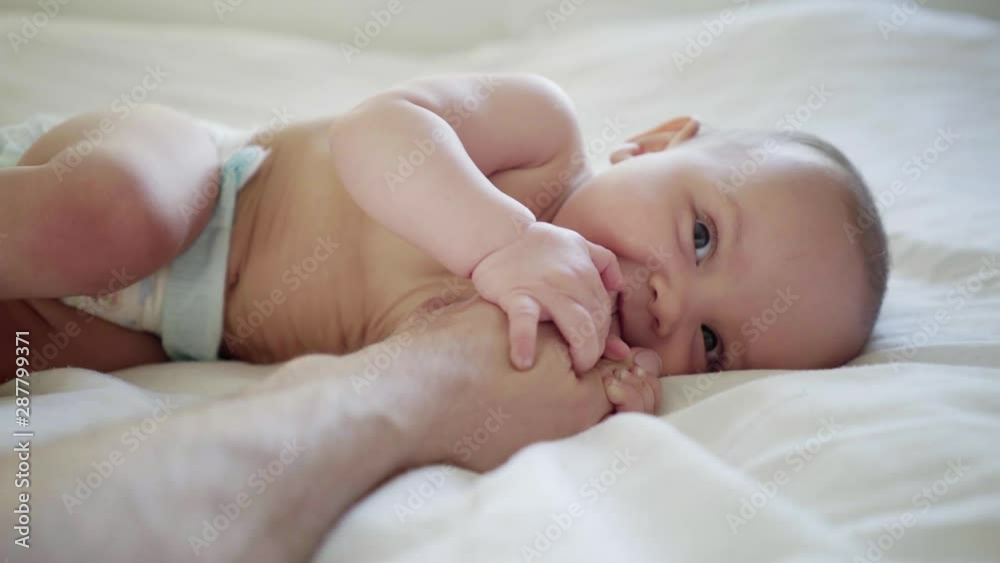 Baby crawls on the bed, smiles, cut his teeth, bites dad by the finger Baby crawls on the bed, smiles, cut his teeth, bites dad by the finger