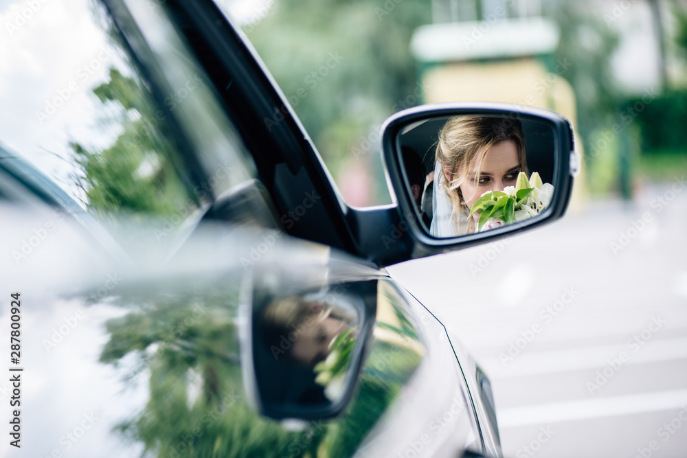 reflection of attractive and blonde bride smelling bouquet in car - obrazy, fototapety, plakaty 