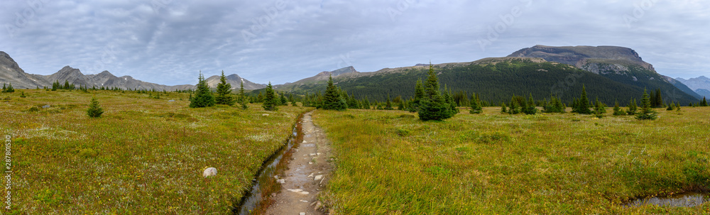 Hiking trail through a panoramic Rocky Mountain landscape with a white clouds, mountains and hills. Hiking trail through a panoramic Rocky Mountain landscape with a white clouds, mountains and hills.