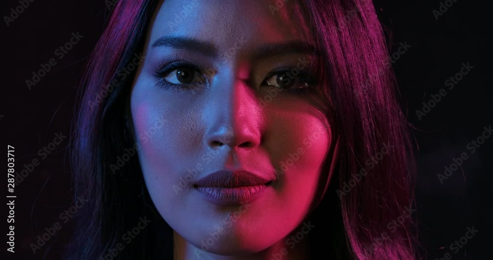 Close up Portrait shot of young flirting cute asian woman playfully posing for camera on the pink and blue neon lights in slow motion. 