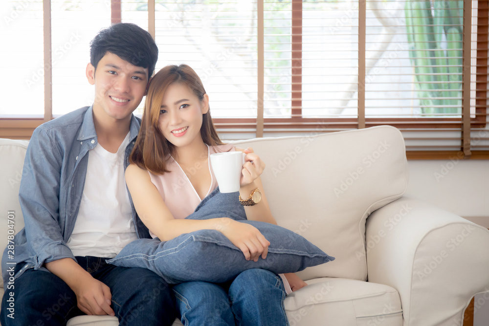 Beautiful young asian couple smiling and talking story married sitting on sofa at home together with woman holding a cup of coffee, man and woman relax and enjoy, lifestyle concept. Beautiful young asian couple smiling and talking story married sitting on sofa at home together with woman holding a cup of coffee, man and woman relax and enjoy, lifestyle concept.
