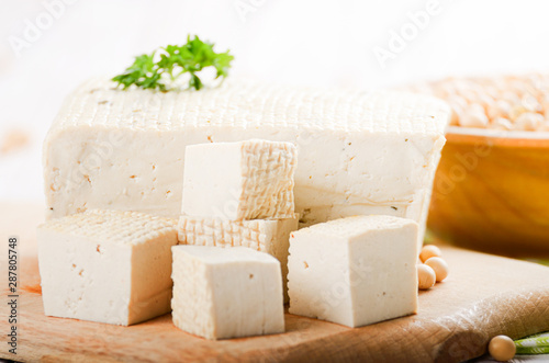 Soy Bean curd tofu on cutting board with bowl of beans aside. Non-dairy alternative substitute for cheese