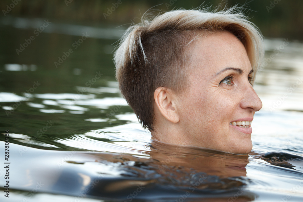 Fototapeta premium Close-up of a woman blonde middle-aged nude swims in the river, selective focus