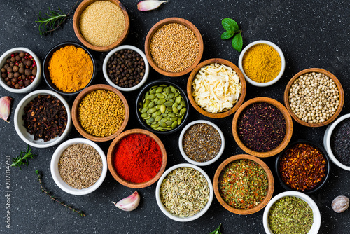 Variety of colorful spices, herbs, and seeds on black stone background © Aleksandr Vorobev