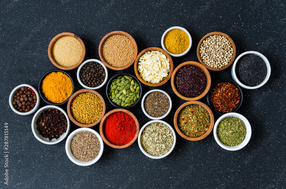 Variety of colorful spices, herbs, and seeds on black stone background