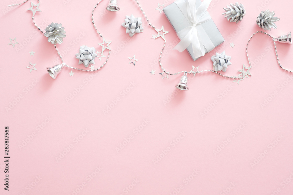 Christmas decorations, stylish silver gift box, pine cones, ribbon, confetti on pastel pink background. Minimal flat lay style composition, top view, copy space. Christmas fashion glamour concept