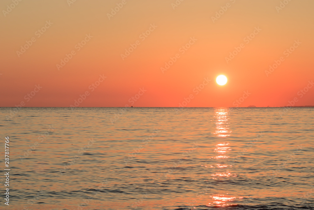 the sun sets on the horizon in the ocean, reflections on the water