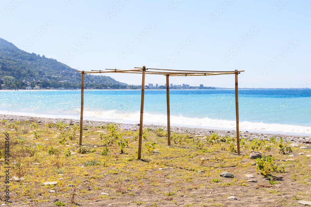 the frame of a wooden structure on the beach against the background of mountains and blue sky