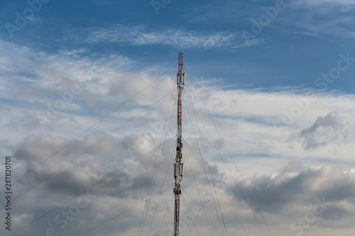 There is a gray and red Radio relay tower with group of different cellular and satellite antennas on the blue sky with white clouds background photo