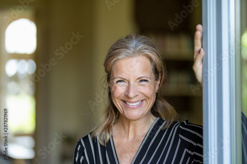 Portrait of smiling mature woman standing at opened terrace door photo