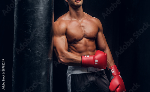 Attractive sporty man is posing with punching bag in dark photo studio. © Fxquadro