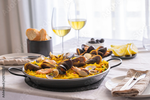 Seafood Paella with  prawns, clams, mussels on saffron rice and vegetables and  bottle of white wine on restaurant table. photo