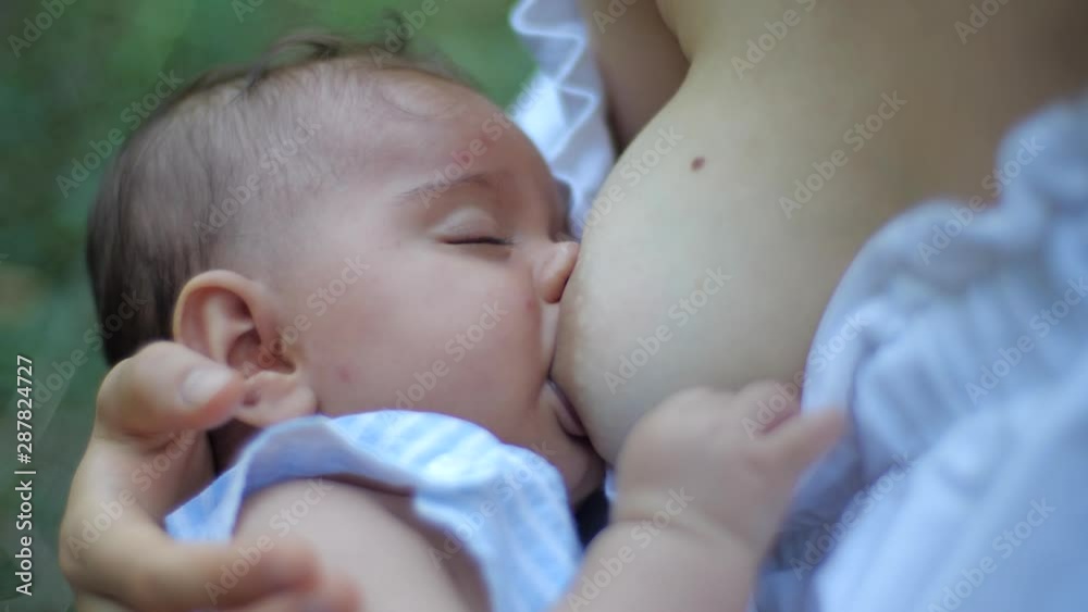 Young beautiful mother, breastfeeding her newborn baby girl outdoors. Mom breastfeeding infant Young beautiful mother, breastfeeding her newborn baby girl outdoors. Mom breastfeeding infant