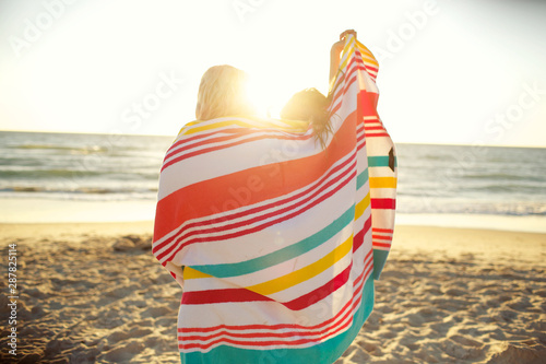 Two girls standing on beach sharing beach towel photo